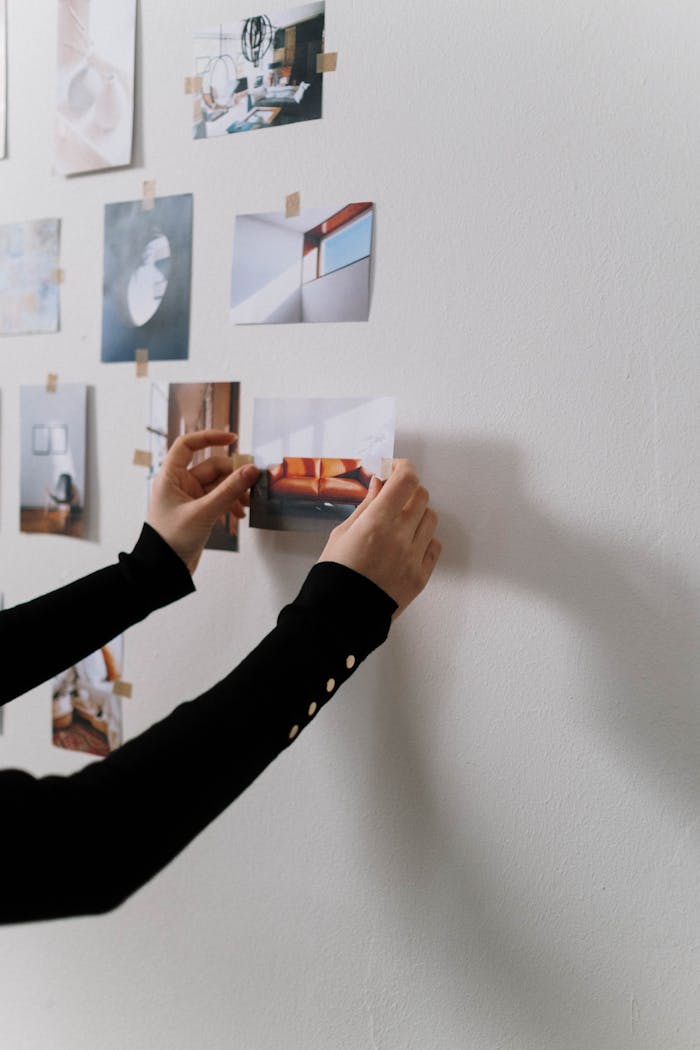 A person arranging photographs on a white wall, showcasing a minimalist design.